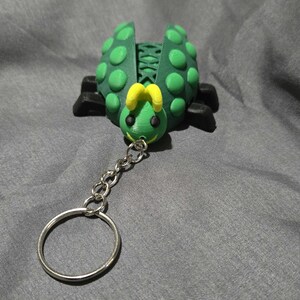 May include: A green and yellow ladybug keychain with a silver chain and ring. The ladybug has a smiling face and yellow antennae.
