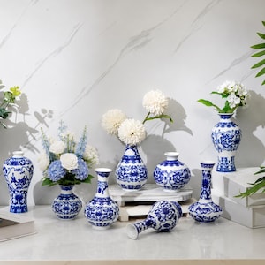 May include: A collection of blue and white ceramic vases featuring intricate floral and scroll patterns. The set includes various shapes, such as bulbous, slender, and flared designs, some holding artificial white and blue flower arrangements.