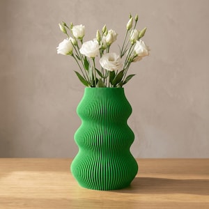 May include: A vibrant green vase with a distinct ribbed, undulating texture and a wide, rounded silhouette. The vase is filled with a bouquet of white lisianthus flowers featuring delicate petals and green stems, creating a contrast.