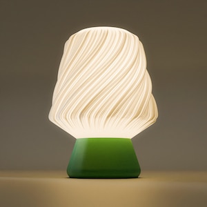 May include: A modern table lamp with a white, swirling shade and a green base. The shade has a textured, layered design, and the base is a solid, trapezoidal shape. The lamp emits a soft, warm glow, creating a cozy ambiance.