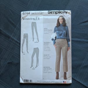May include: A Simplicity 8744 Amazing Fit sewing pattern envelope for trousers in sizes 10-18. The front shows a model wearing tan houndstooth trousers with a wide waistband and invisible zipper, alongside illustrations for average, slim, and curvy fits.