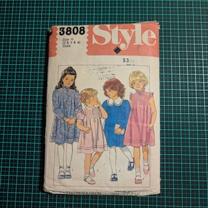 May include: A vintage Style 3808 sewing pattern for children's dresses. The cover shows illustrations of four girls in different dresses. The cover is pink and white, with the text "Style" and "3808". The price is $3.25.