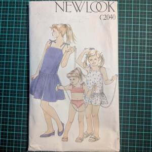 May include: A vintage sewing pattern for girls' clothing, featuring three girls wearing different outfits. The pattern is from New Look and has the number C2040 printed on it.