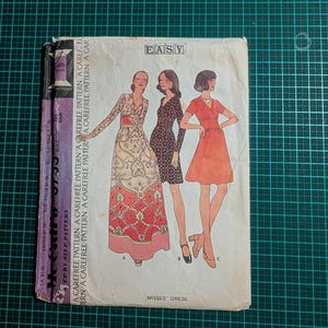 May include: A vintage sewing pattern for Misses' dresses. The cover shows illustrations of three dress designs. The pattern is labelled "Easy" and includes the text "Misses' Dress". The pattern is on a green cutting mat.