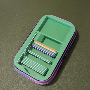 Op de afbeelding: Een groene en paarse opbergdoos met een vak voor kaarten. De doos bevat kaarten in regenboogkleuren.