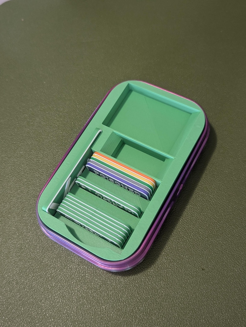 Op de afbeelding: Een groene en paarse opbergdoos met een vak voor kaarten. De doos bevat kaarten in regenboogkleuren.