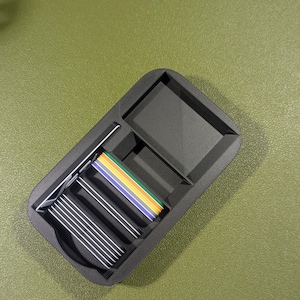 Op de afbeelding: Een zwarte plastic organizer met meerdere vakken. De organizer bevat een stapel zilveren kaarten en een kleurrijk lint.