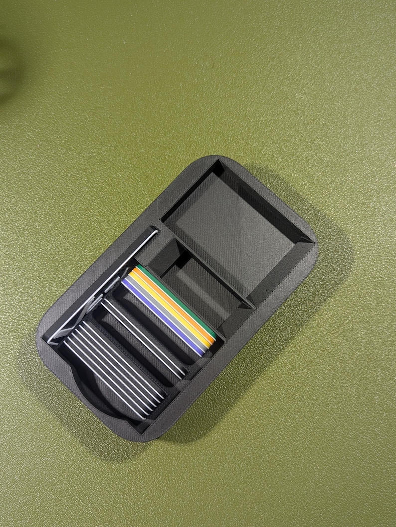 Op de afbeelding: Een zwarte plastic organizer met meerdere vakken. De organizer bevat een stapel zilveren kaarten en een kleurrijk lint.