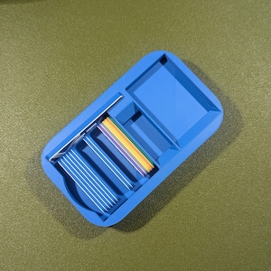 Op de afbeelding: Een blauwe plastic organizer met meerdere vakken. De organizer heeft een regenboogkleurig lint erin.