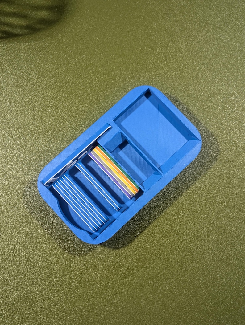 Op de afbeelding: Een blauwe plastic organizer met meerdere vakken. De organizer heeft een regenboogkleurig lint erin.