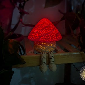 May include: A red and white mushroom-shaped lamp with a dotted pattern on the top and a white base with legs. The lamp is lit and casting a warm glow.