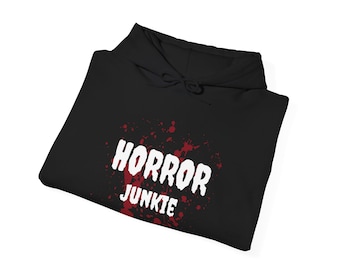 Pode incluir: Moletom preto com a inscrição branca "HORROR JUNKIE" sobre um design de respingos vermelhos. O moletom tem capuz com cordão e está dobrado.