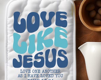 May include: White quilted pot holder with the text "LOVE LIKE JESUS" in blue and teal. The pot holder also has the text "LOVE ONE ANOTHER AS I HAVE LOVED YOU JOHN 13:34". A white loop is attached for hanging.