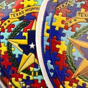 Puede incluir: Dos parches circulares con un patrón de piezas de rompecabezas en rojo, azul, amarillo y azul claro. Cada parche muestra una estrella dorada central, una corona de laurel verde y una cinta amarilla con el texto TEXAS HIGHWAY PATROL.