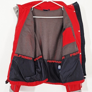 May include: A red and black jacket with the interior visible, hanging on a white hanger. The jacket has the words "HILFIGER" and "FERRARI" in red lettering. The interior is a dark mesh material.