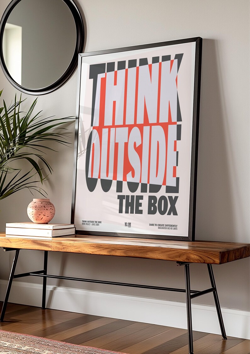 Op de afbeelding: Een ingelijste poster met de woorden "THINK OUTSIDE THE BOX" in vette, witte en rode letters. De poster wordt weergegeven op een houten bank met zwarte metalen poten. Een ronde spiegel en een plant zijn zichtbaar op de achtergrond.