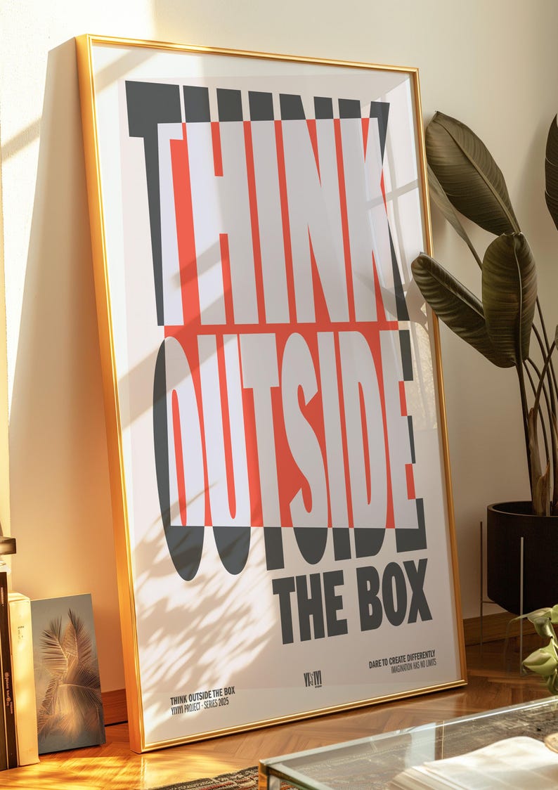 Op de afbeelding: Een ingelijste poster met de tekst "THINK OUTSIDE THE BOX" in een gedurfde, moderne lettertype. De tekst is wit, rood en grijs op een cr&egrave;mekleurige achtergrond. De poster zit in een gouden lijst en staat tegen een muur.