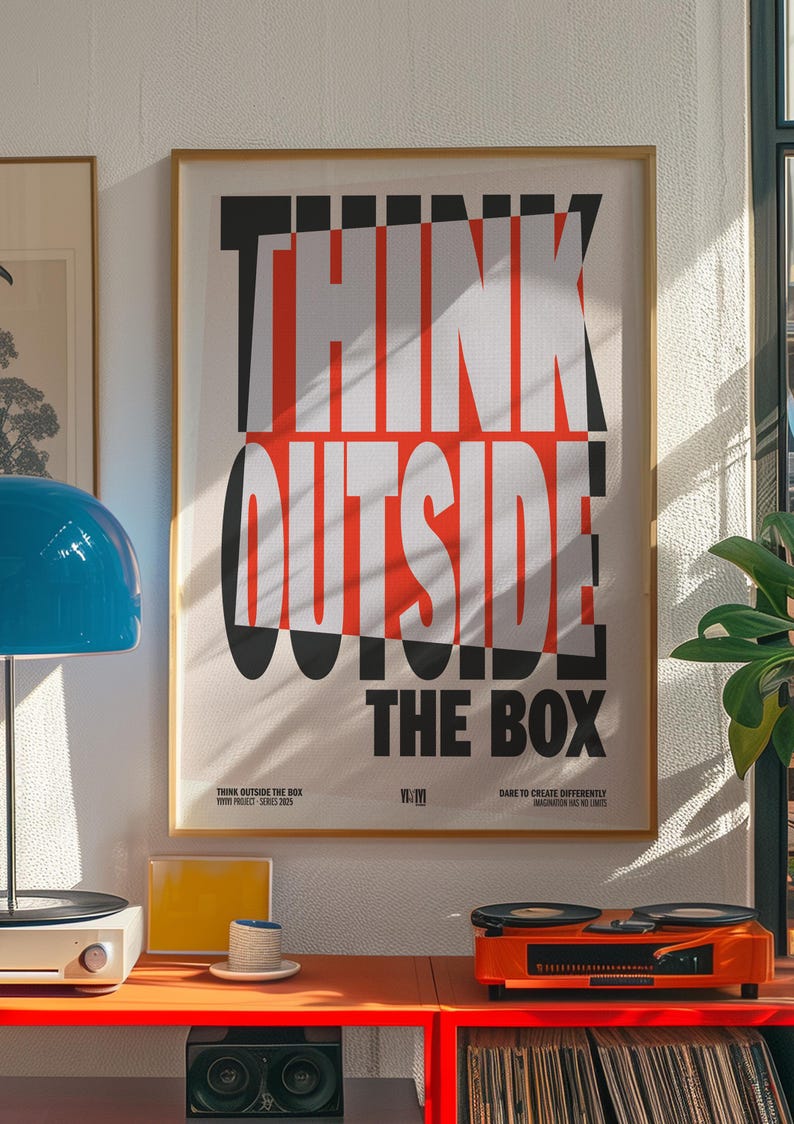 Op de afbeelding: Een ingelijste poster met de tekst "THINK OUTSIDE THE BOX" in een vet, modern lettertype. De poster heeft een cr&egrave;mekleurige achtergrond met zwarte en rode letters. De afbeelding toont ook een blauwe lamp, een platenspeler en andere decoratieve items.
