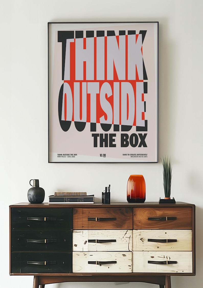 Op de afbeelding: Een ingelijste poster met de woorden "THINK OUTSIDE THE BOX" in vetgedrukte, gestileerde letters. Boven een houten dressoir met diverse decoratieve items, waaronder een vaas en een kleine plant. Het dressoir heeft lades in zwart, wit en houttinten.