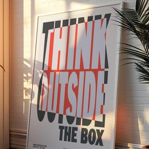 Op de afbeelding: Een ingelijste poster met de woorden "THINK OUTSIDE THE BOX" in grote, vette, witte en rode letters. De poster leunt tegen een witte bakstenen muur, met schaduwen van zonlicht.