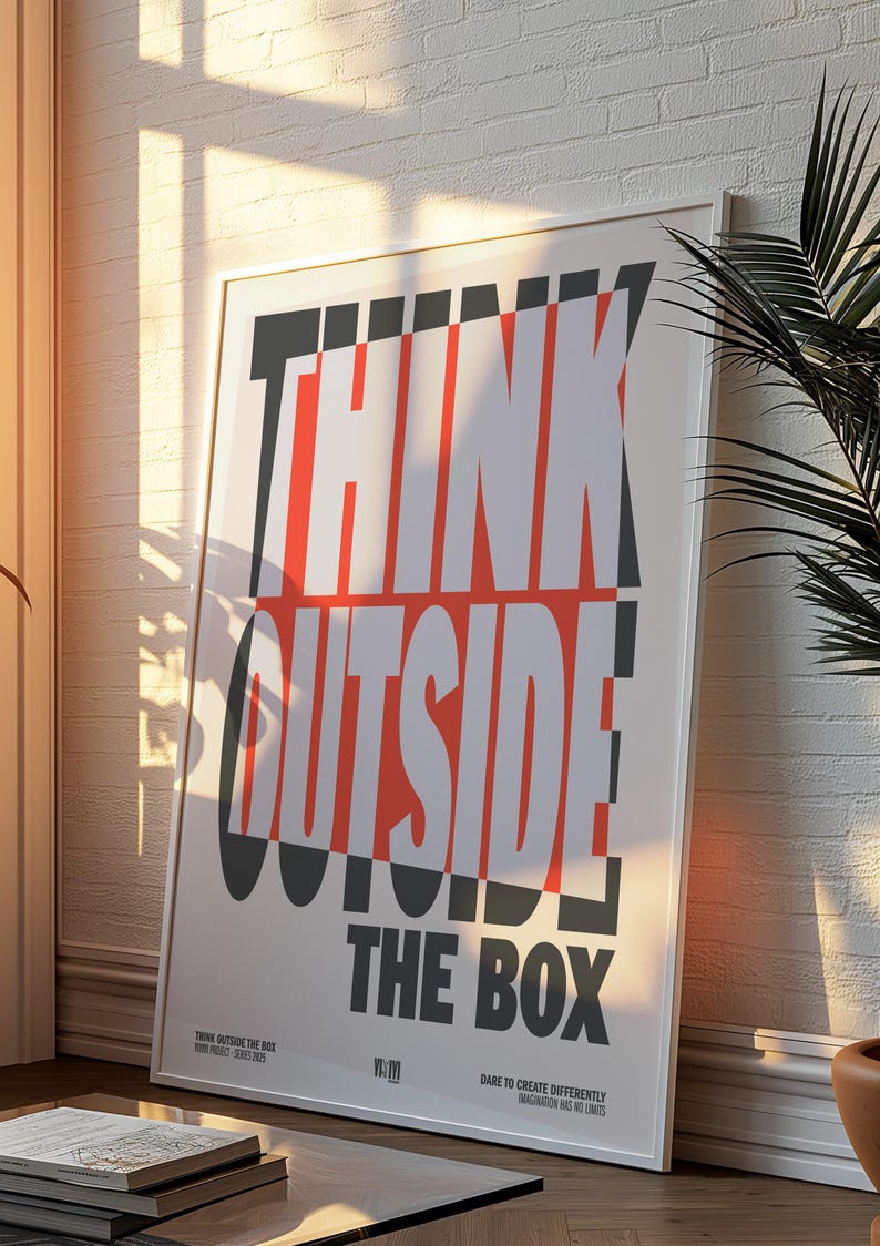 Op de afbeelding: Een ingelijste poster met de woorden "THINK OUTSIDE THE BOX" in grote, vette, witte en rode letters. De poster leunt tegen een witte bakstenen muur, met schaduwen van zonlicht.