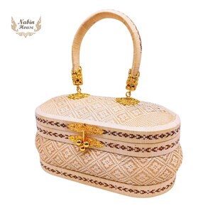 May include: A woven oval-shaped handbag with a gold handle and clasp. The bag has a brown and white geometric pattern.