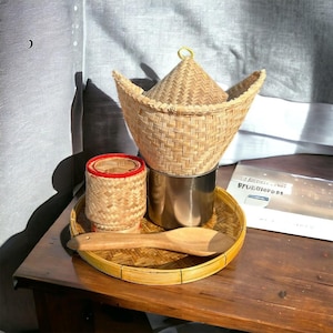 May include: A collection of woven bamboo food containers and serving utensils. The set includes a large conical basket, a small cylindrical container with a red rim, a round tray, and a wooden spoon. The containers sit on a wooden table.
