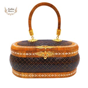 May include: A woven oval-shaped handbag with a brown and black pattern. The handbag has a gold-colored handle and clasp. The handbag is made of natural materials.