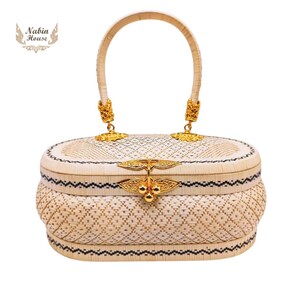 May include: A white woven oval handbag with a gold handle and clasp. The bag has a black and white geometric pattern.