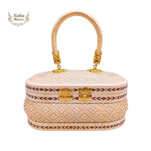 May include: A white woven handbag with a gold handle and gold clasps. The bag has a brown trim and a woven pattern.