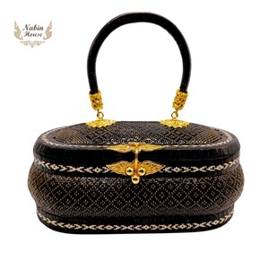 May include: A black woven handbag with a gold handle and decorative accents. The bag has a woven pattern and a white trim.