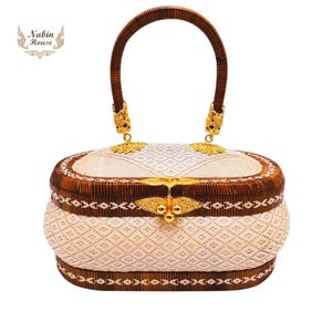 May include: A white and brown woven handbag with a gold clasp and handle. The bag has a traditional woven pattern and is decorated with gold accents.