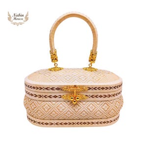 May include: A white woven handbag with a gold handle and a gold clasp. The bag has a geometric pattern and a brown trim.