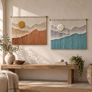 May include: Two rectangular macrame wall hangings featuring layered fibre landscapes. The left piece displays warm tones of cream, tan, and rust with a textured yellow circle. The right piece features cool shades of cream, grey, and teal with a white circle.