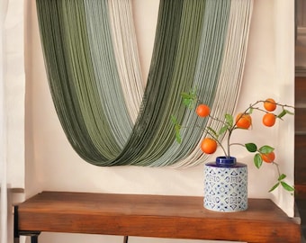May include: Two wall hangings with a gradient of green and white threads are mounted on wooden bars. A wooden table holds a blue and white patterned vase with orange fruit branches.