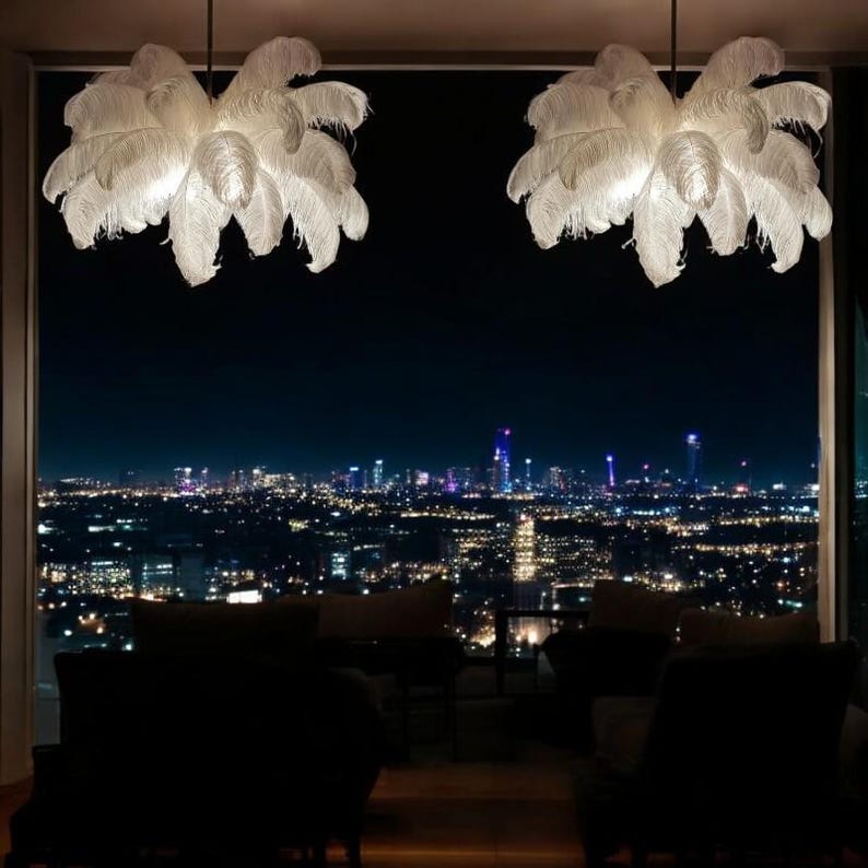 K&ouml;nnte beinhalten: Zwei wei&szlig;e Federleuchter h&auml;ngen von der Decke eines Raumes mit einem gro&szlig;en Fenster, das einen Blick auf die n&auml;chtliche Skyline der Stadt bietet.