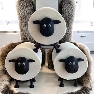 May include: Three sheep-shaped stools. Each stool has a white, circular seat with a black sheep face and legs. The sheep have large, round eyes and black ears. The stools are grouped together, creating a playful and decorative element for a room.