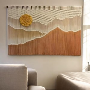 Peut inclure: Une tapisserie murale en macramé avec un soleil jaune et des nuages blancs sur un fond brun.