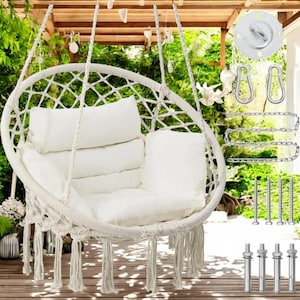 May include: White hanging hammock chair with fringe, featuring a white cushion and two back pillows. The chair is suspended from a wooden ceiling and includes hanging hardware.