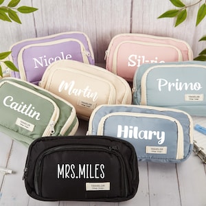 May include: A selection of personalised travel pouches in pastel shades like lavender, pink, and green. Each pouch features a name printed in white, with a small "Traveler" label.