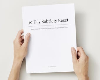 Pode incluir: Um caderno branco intitulado "30 Day Sobriety Reset" com o subtítulo "A simple daily workbook for grounding and reflection". O livro é segurado aberto por duas mãos. A marca "GroundedDays" está impressa na parte inferior.