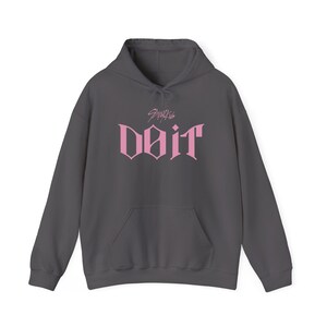 May include: A charcoal gray hoodie with a front pocket and drawstring hood. The front features the pink text "doit" in a stylized font, with the text "Stray Kids" above it. The hoodie is a casual garment.