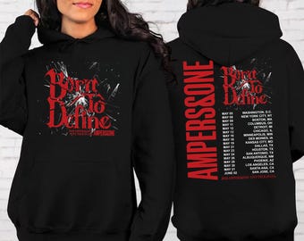 May include: Black hoodie featuring the text "Born to Define" in red, with "AMPERSSONE" on the front and back. The back also lists tour dates and locations. The hoodie has a hood and a front pocket.