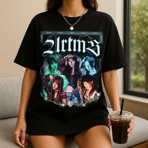 May include: Black t-shirt featuring a graphic design with the word "2lrtm3" in a stylized font. The design includes images of several people. The shirt has a crew neck and short sleeves.