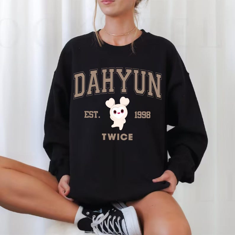 May include: Black sweatshirt featuring the name "DAHYUN" in a tan collegiate font. Below the name is "EST. 1998" and the word "TWICE". A white cartoon character with heart-shaped eyes is in the center.