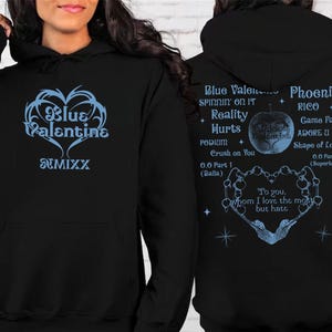 May include: Black hoodie with a light blue graphic on the front that says "Blue Valentine" and "NMIXX". The back of the hoodie has a list of song titles and lyrics in light blue. The hoodie has a front pocket and a hood.