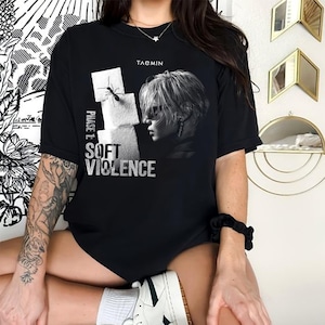 May include: A black short-sleeve t-shirt featuring a graphic print of a person in profile, a stack of white sugar cubes with an ant on top, and the text "TAEMIN" and "PHASE 1: SOFT VIOLENCE" printed in white on the front of the garment.