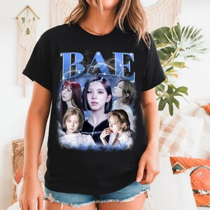 May include: Black t-shirt featuring a graphic design with the word "BAE" in blue, with a group of women's faces in the center. The design has a vintage, faded aesthetic. The shirt is short-sleeved.