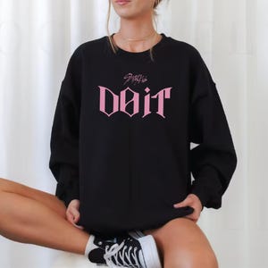 May include: Black sweatshirt with the pink text "Do It" in a gothic font. Above the text is the name "Stray Kids". The sweatshirt is worn by a person.