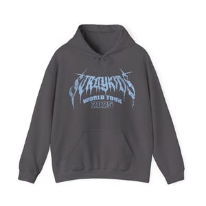 Puede incluir: Una sudadera con capucha gris oscuro con un bolsillo delantero y una capucha con cord&oacute;n. La parte delantera presenta el texto "Stray Kids World Tour 2025" en azul claro, con una fuente estilizada. La sudadera est&aacute; hecha de un material suave.